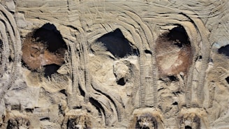 Aerial view of construction site soil with distinct tire tread patterns and uneven terrain. The surface shows a variety of textures and shades, primarily composed of light earth tones.