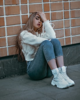 a woman sitting on the ground next to a brick wall