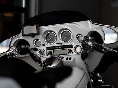 The image displays the dashboard of a motorcycle, including a set of analog gauges, a small digital screen, and multiple control buttons. The handlebars and mirrors are visible, with chrome detailing and a sleek, modern design.