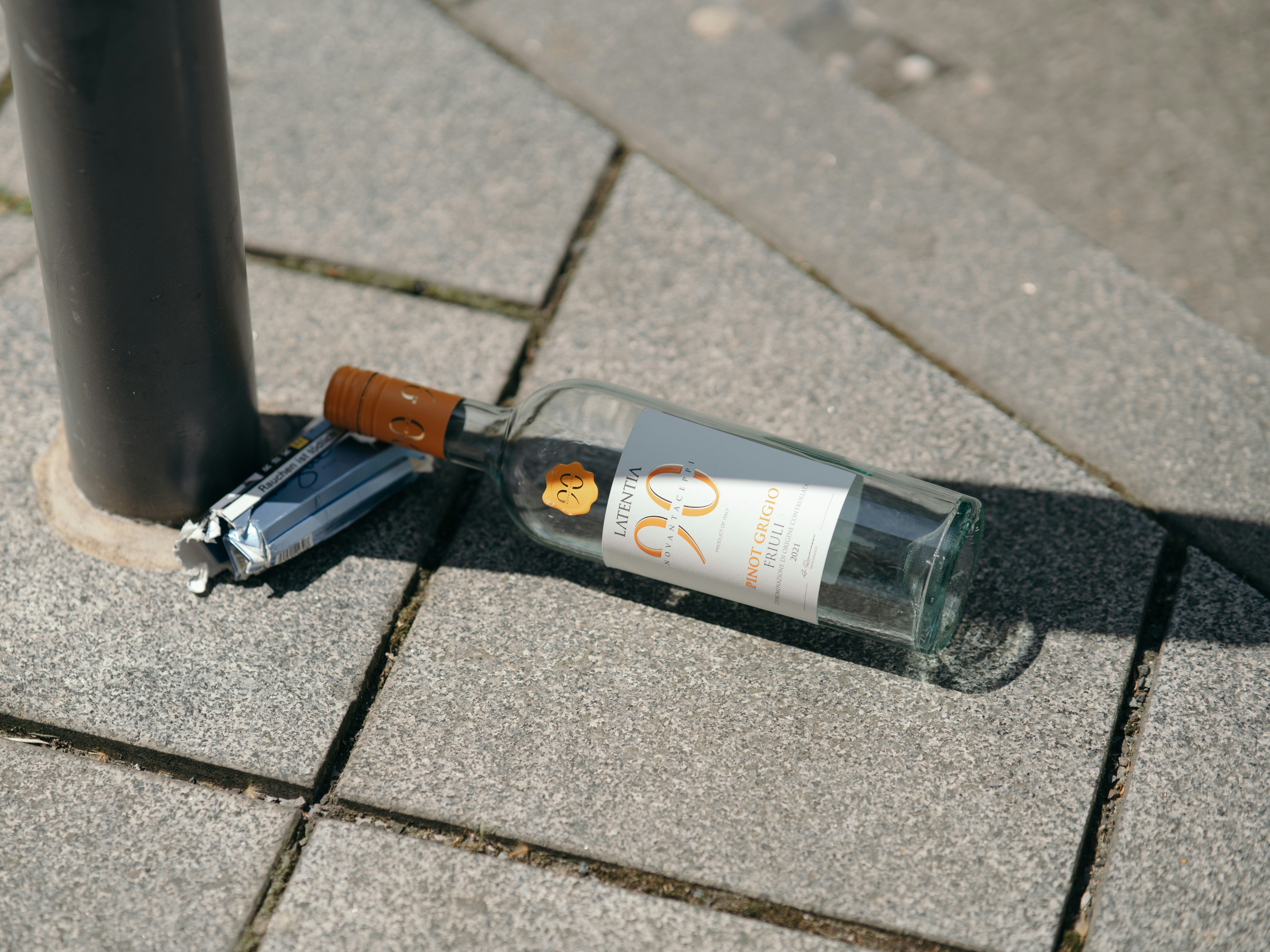 a bottle of wine sitting on the ground next to a pole