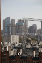 Skyscrapers dominate the skyline in the background, while several construction cranes and residential buildings occupy the foreground. The mix of modern and older structures creates a sense of urban development and growth.