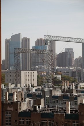 Skyscrapers dominate the skyline in the background, while several construction cranes and residential buildings occupy the foreground. The mix of modern and older structures creates a sense of urban development and growth.
