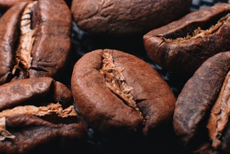 Close-up view of several roasted coffee beans with visible texture and details, showcasing their rich brown color and the characteristic line down the center of each bean.
