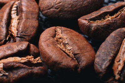 Close-up view of several roasted coffee beans with visible texture and details, showcasing their rich brown color and the characteristic line down the center of each bean.