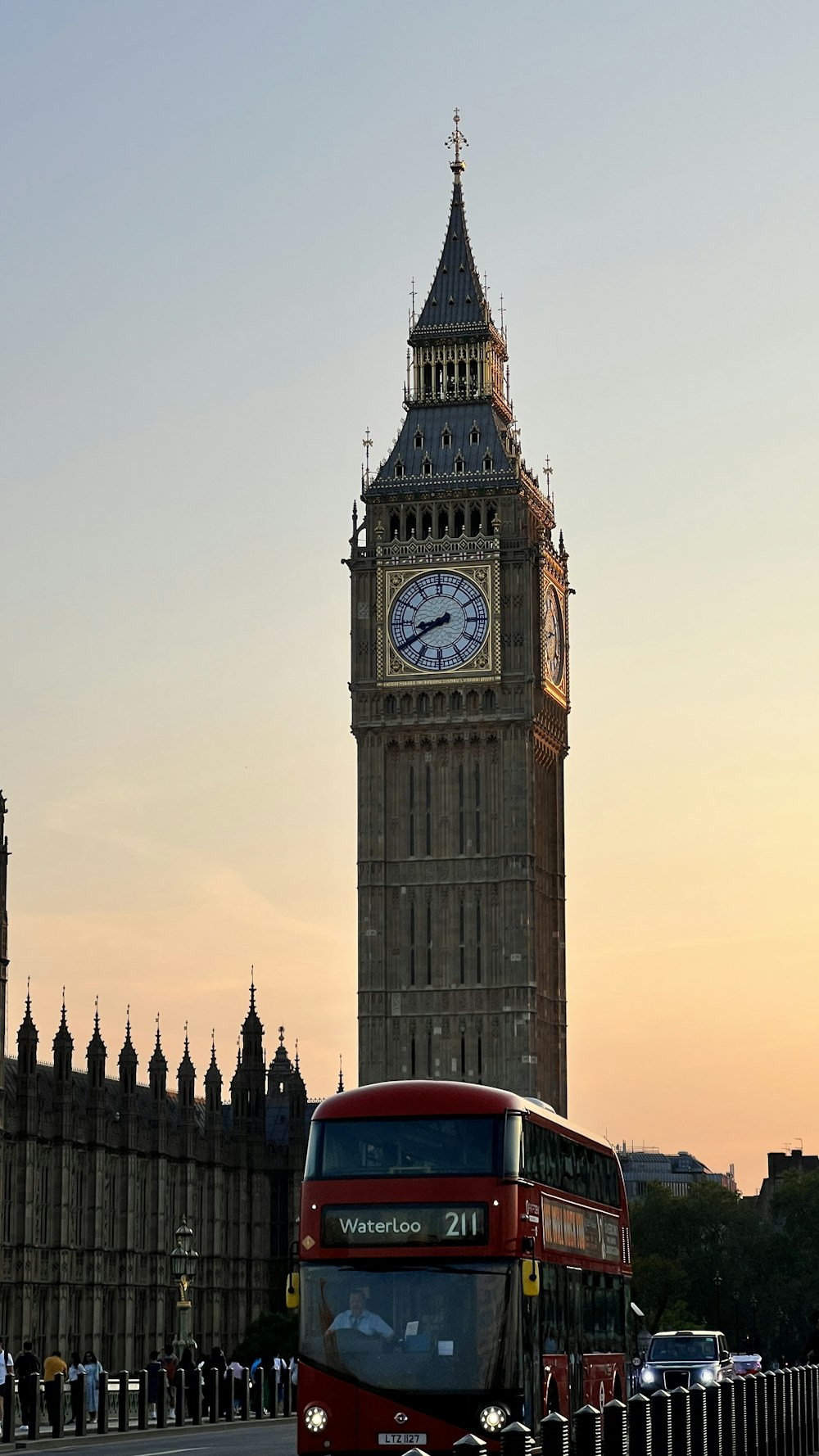 a red double decker bus driving past a tall clock tower