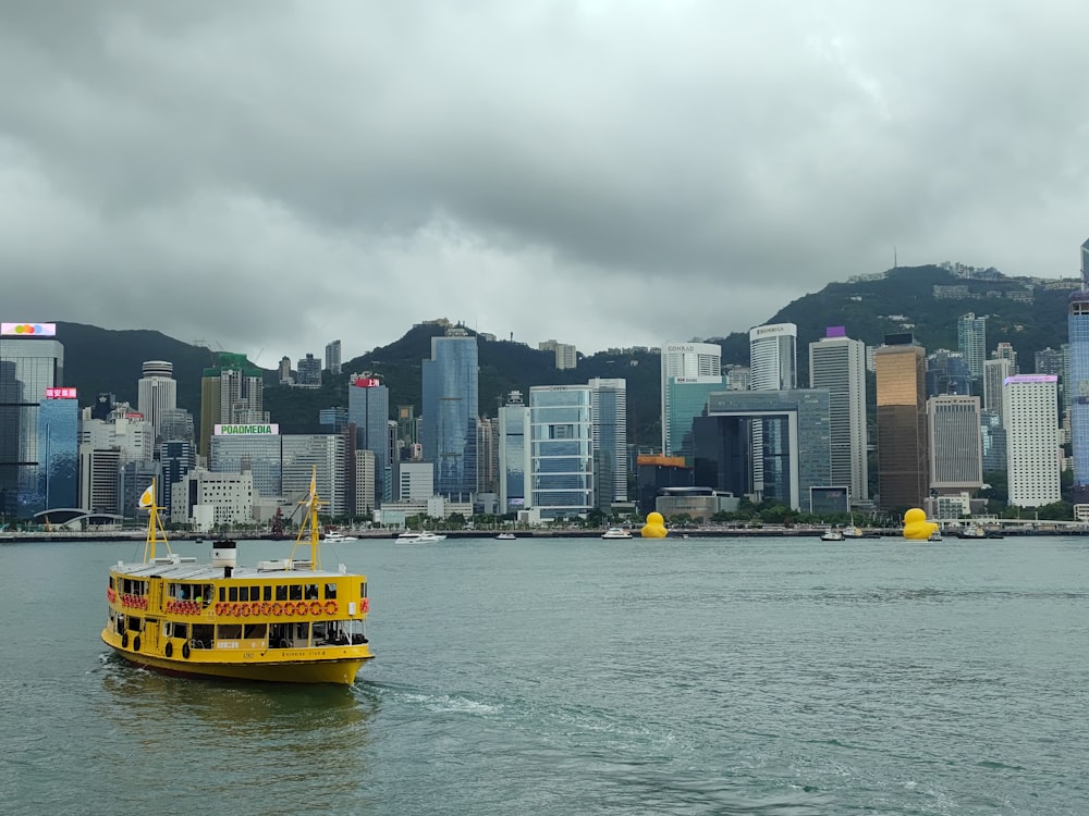 a yellow boat in the water with a city in the background