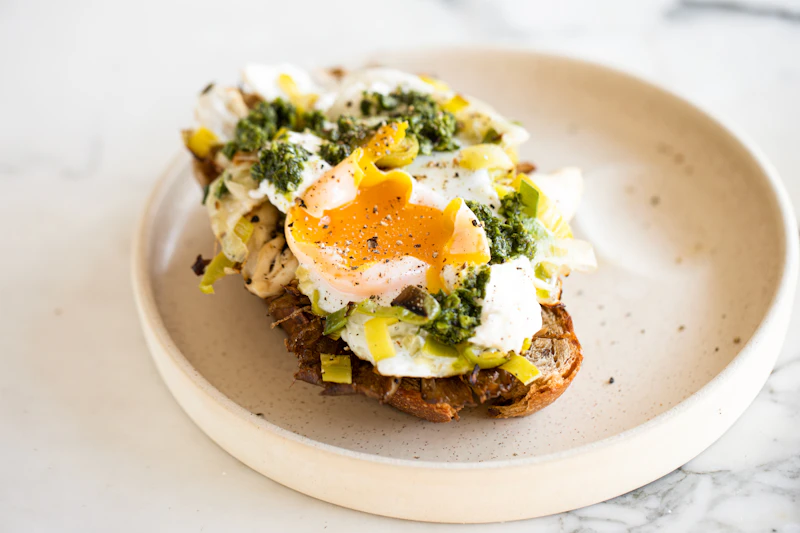 Soft eggs and green herb oil on toasted sourdough, on a pale ceramic plate