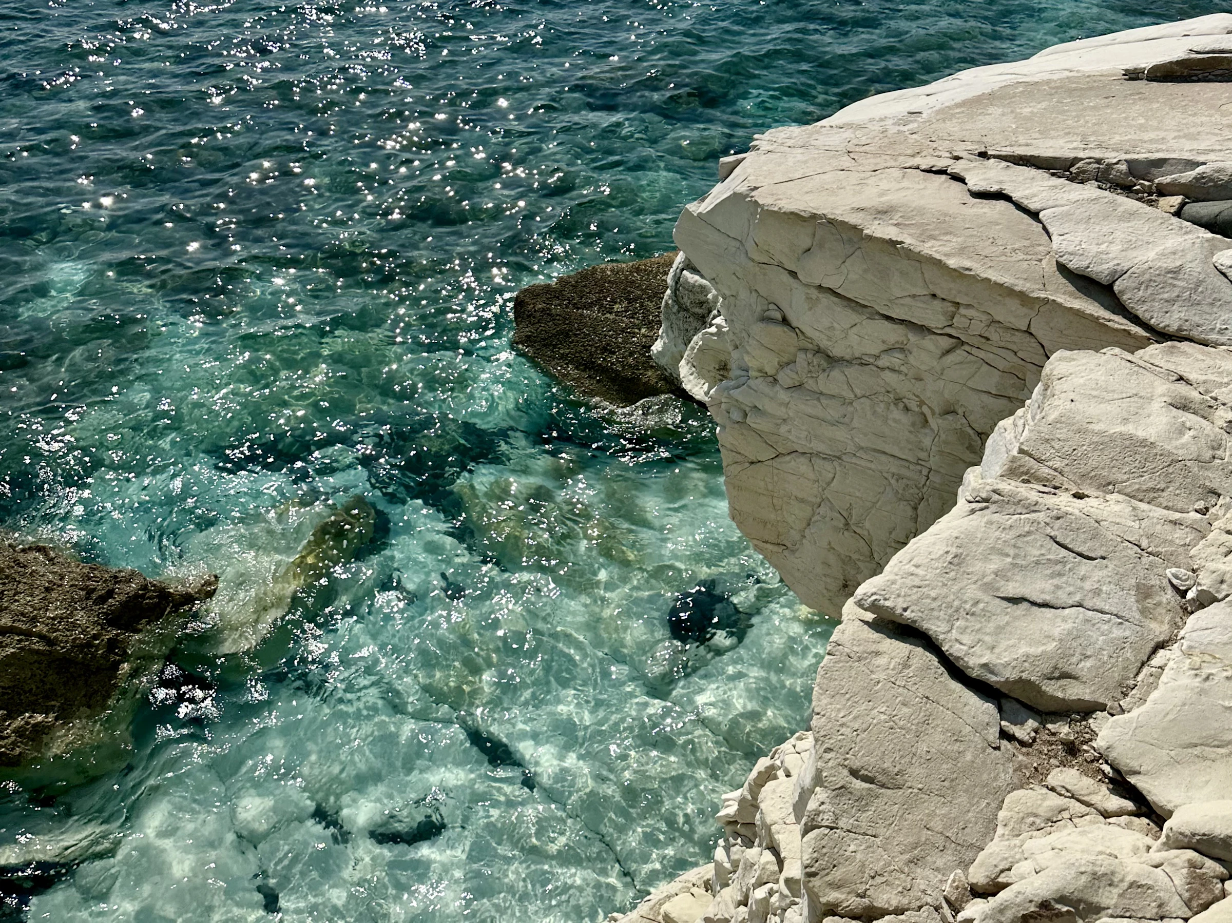 Clear turquoise water washing over a submerged rock shelf beside pale limestone rocks on the Cyprus coast