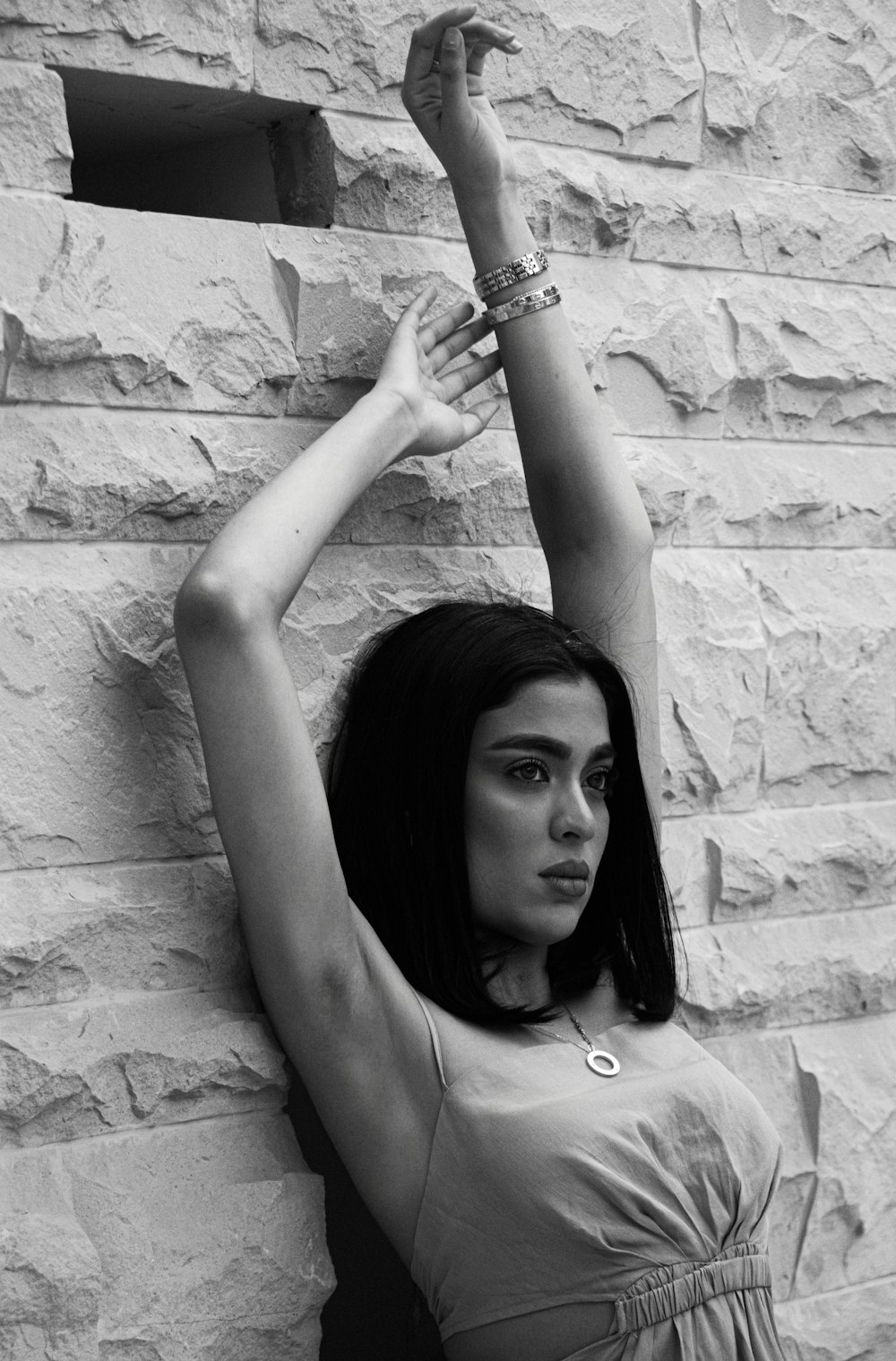 a black and white photo of a woman leaning against a brick wall