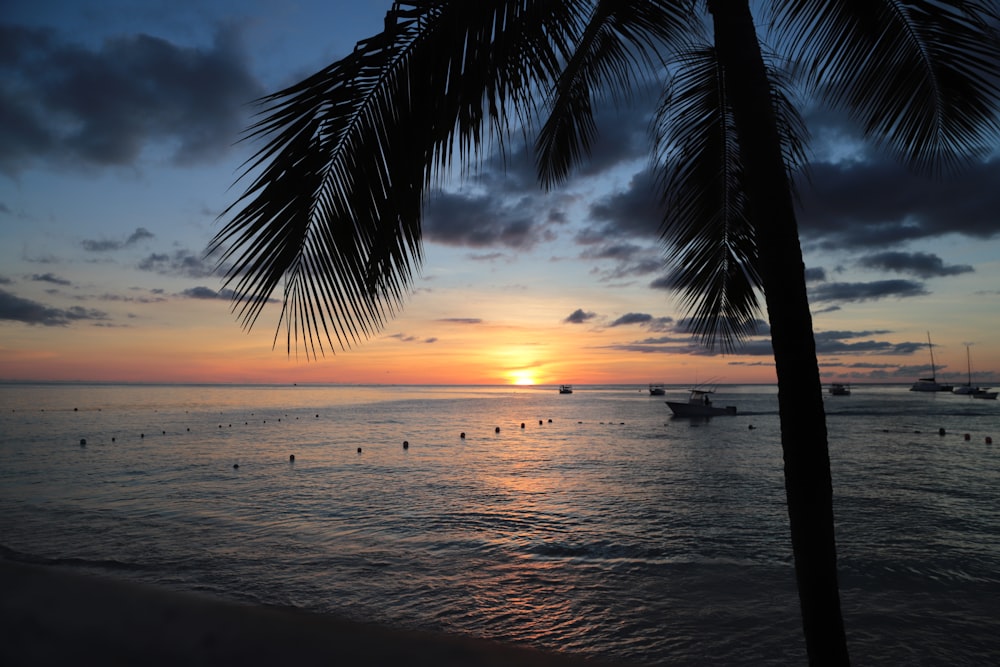 the sun is setting over the ocean with boats in the water