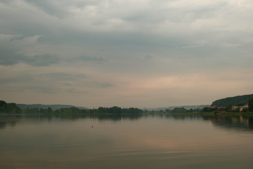 a body of water surrounded by trees under a cloudy sky