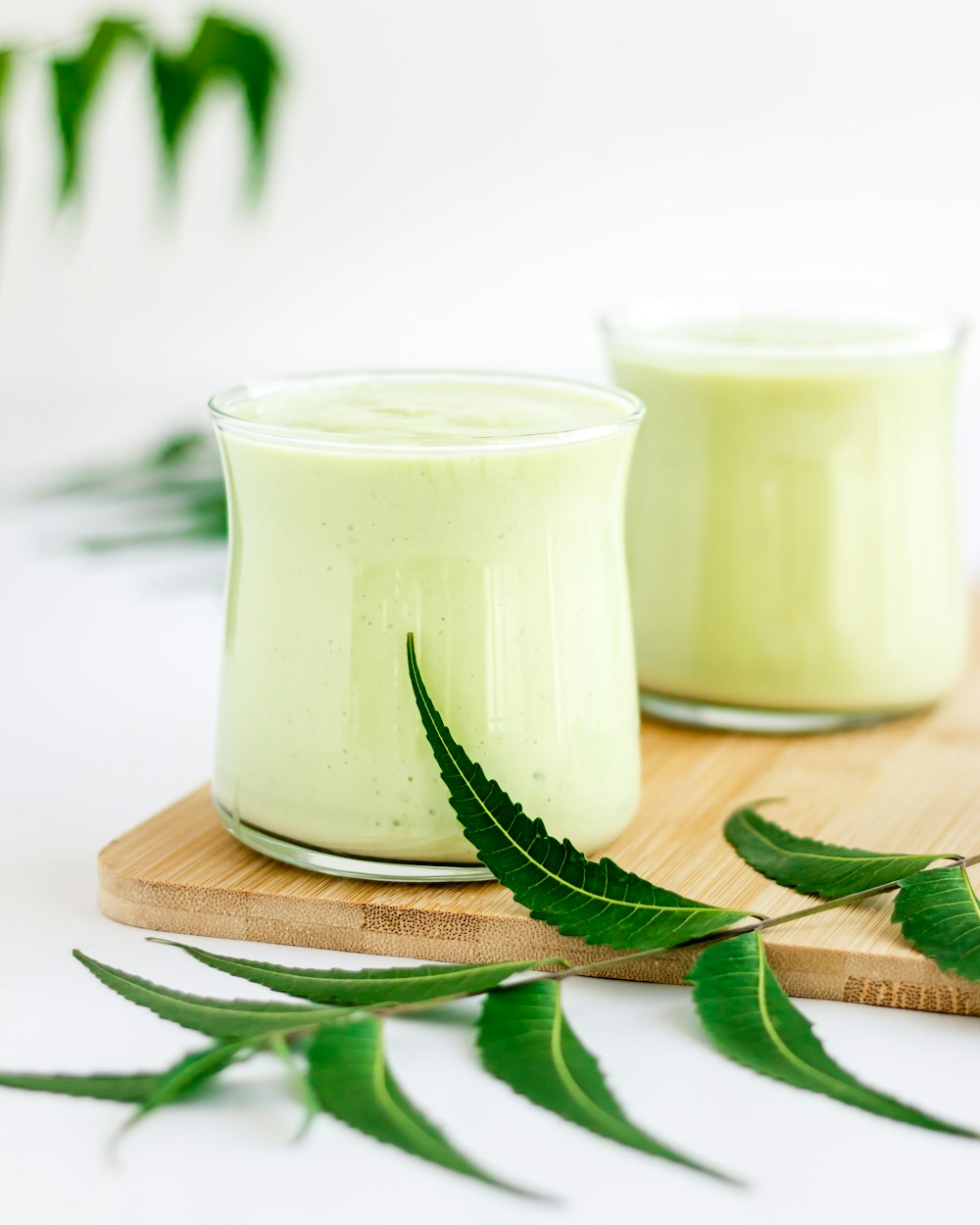 two glasses of green smoothie on a cutting board