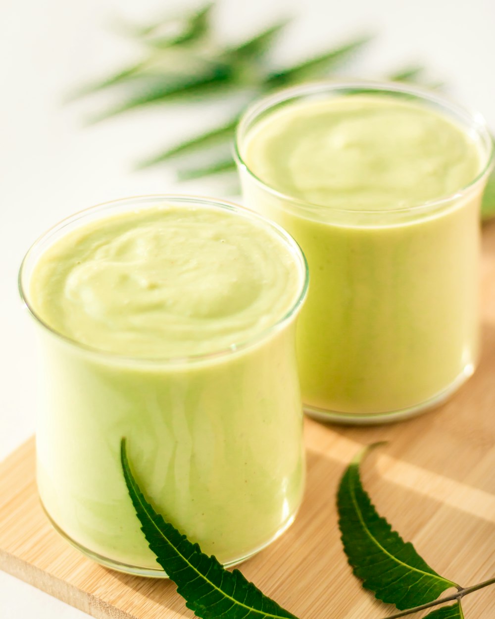 two glasses of green smoothie on a wooden tray