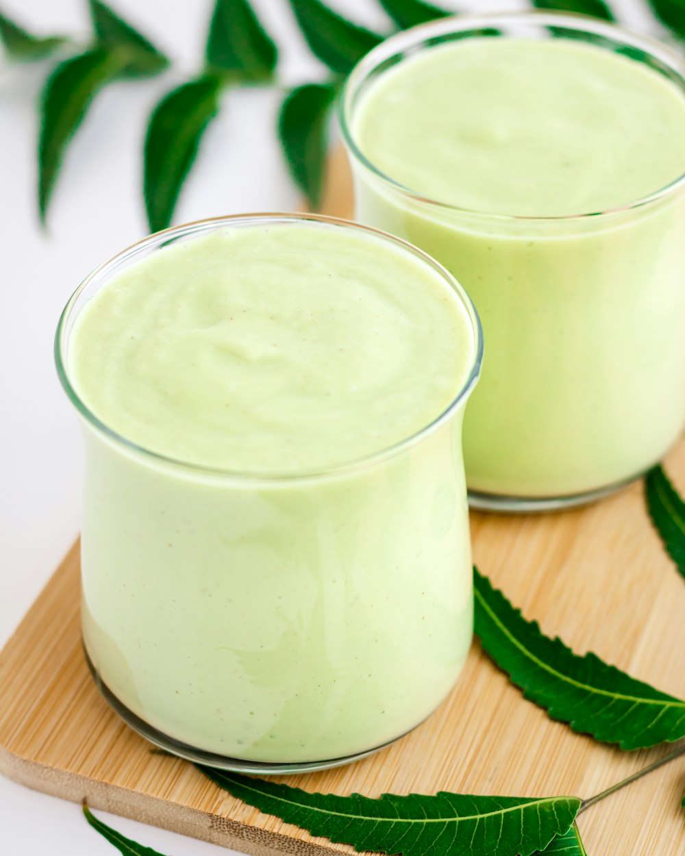 two glasses of green smoothie on a cutting board