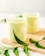 Two glasses filled with a creamy, light green smoothie are placed on a wooden board. Fresh green leaves, likely from a neem plant, are artfully arranged around the glasses, adding a natural and fresh element.