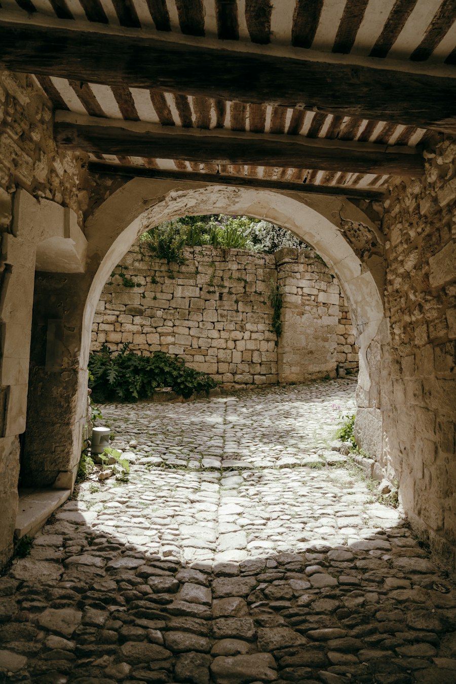 A sunlit stone archway opening onto a cobbled courtyard and an old stone wall