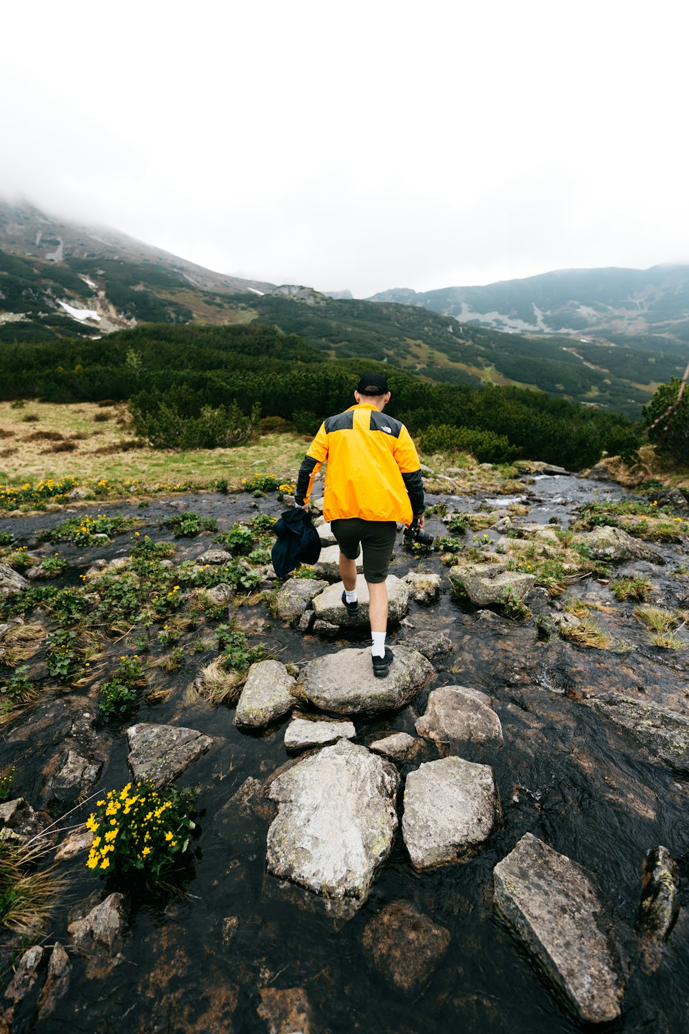 a man in a yellow jacket is walking on rocks