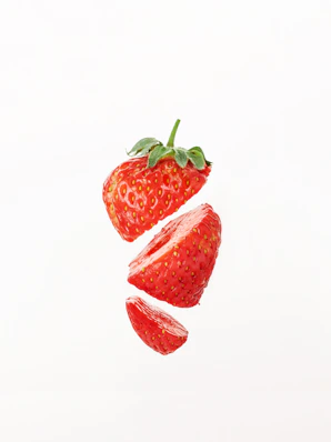 Three sliced pieces of a fresh red strawberry floating against a white background