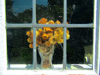 Bright orange ceramic vase holding fresh wildflowers on a windowsill.