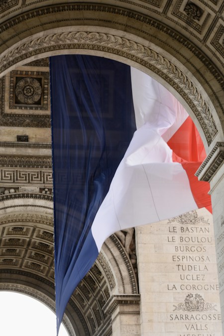 Un grand drapeau tricolore suspendu sous la voûte sculptée de l’Arc de triomphe, à Paris