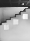 A staircase with a zigzag pattern and three rectangular windows on the adjacent wall. The ceiling features a smoke detector.