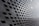 A modern architectural facade featuring a pattern of diamond-shaped openings arranged in a repetitive, grid-like structure. The sleek, metallic surface creates a futuristic and dynamic appearance with alternating light and shadow effects.