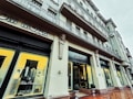 A stylish building with a fashion boutique featuring decorative architectural details. Mannequins displaying suits are visible through large, illuminated windows. The facade has ornamental columns and sculptural elements, with a sign in Cyrillic above the entrance.