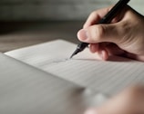 a person writing on a piece of paper with a pen