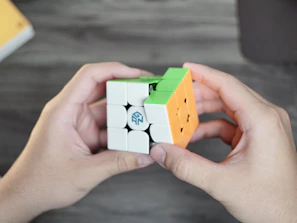 Close-up of hands twisting a speed cube with a focused expression in the background.