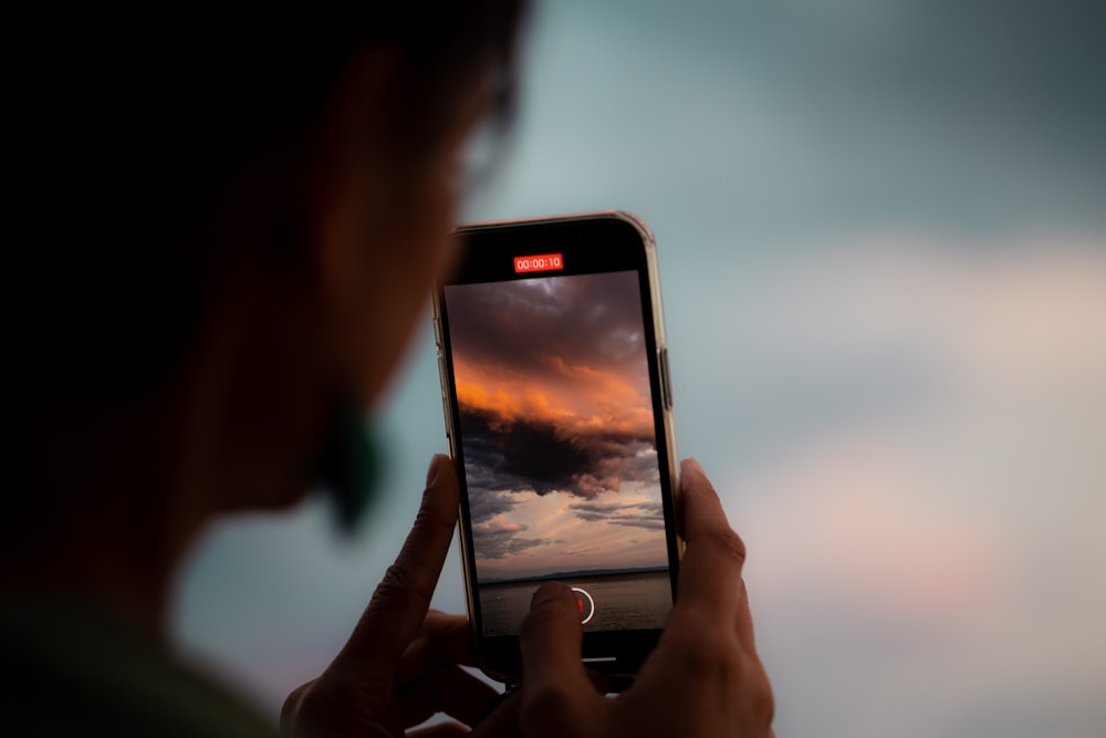 a person taking a picture of a sunset with a cell phone