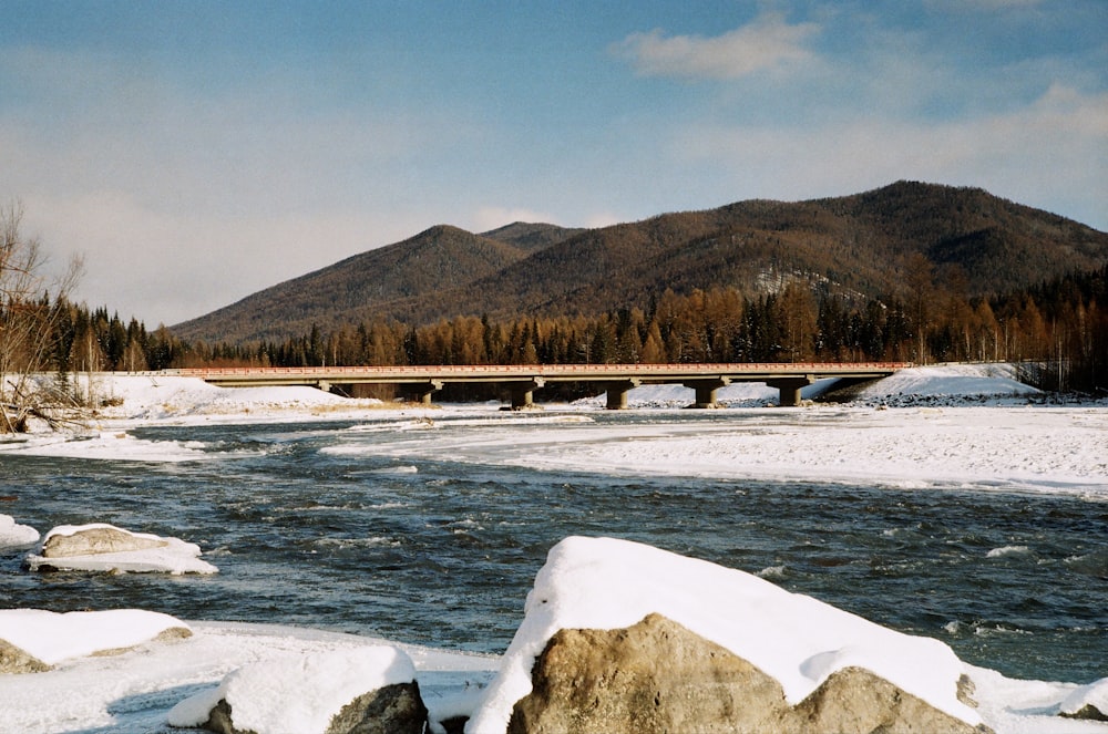 a bridge over a river surrounded by snow covered rocks