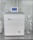 A sleek, modern laboratory water purification system is placed on a stainless steel countertop. The device is predominantly white with a digital control display at the top, featuring the brand logos 'Rephile' and 'Genie'. Surrounding the unit are various laboratory fixtures, including pipes, a pressure gauge, and a clipboard with documentation. A plug with cords is connected on the side, alongside a small transparent container.