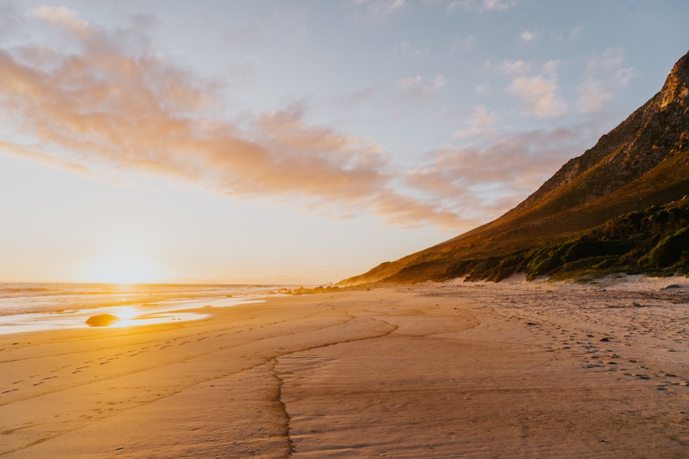 the sun is setting on the beach with footprints in the sand