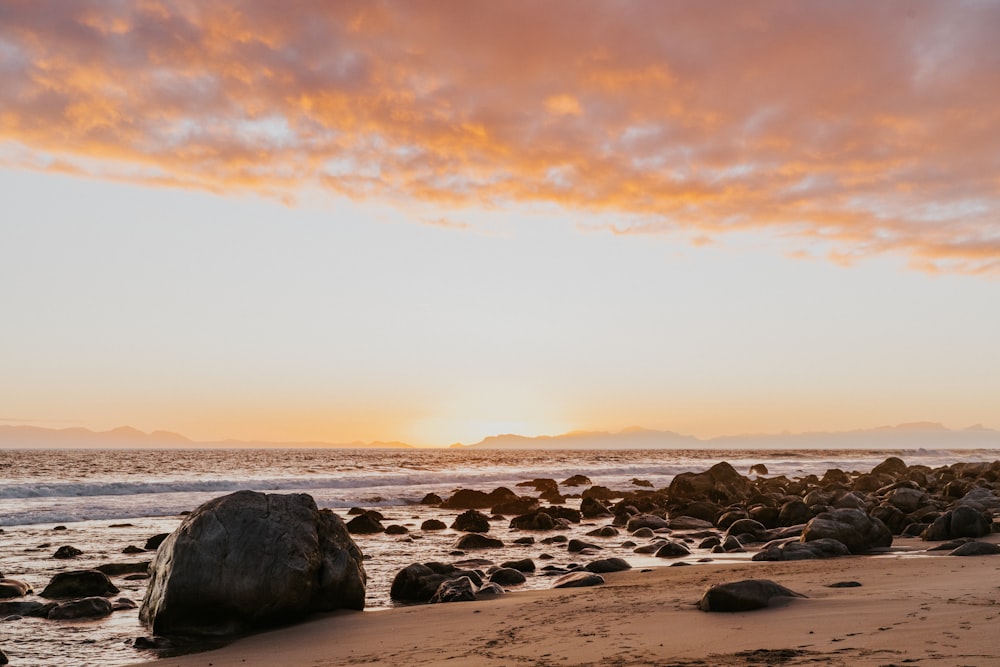 the sun is setting over the ocean with rocks in the foreground