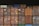 Multiple shipping containers stacked in rows. The containers are of different colors including brown, red, orange, blue, and green, each labeled with various text and symbols. The background is dark, emphasizing the containers.
