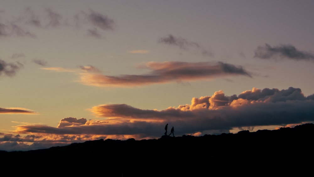 a couple of people standing on top of a hill under a cloudy sky