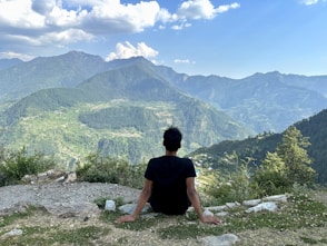 A peaceful individual sitting quietly on a rock, overlooking a lush green valley.