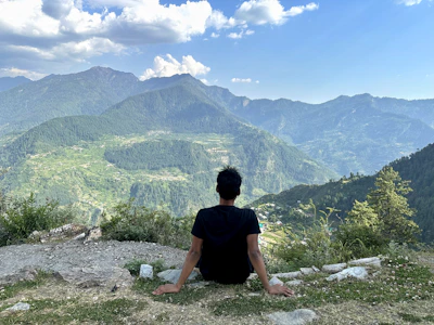 A peaceful traveler sitting quietly on a rocky outcrop, gazing over misty valleys at dawn.