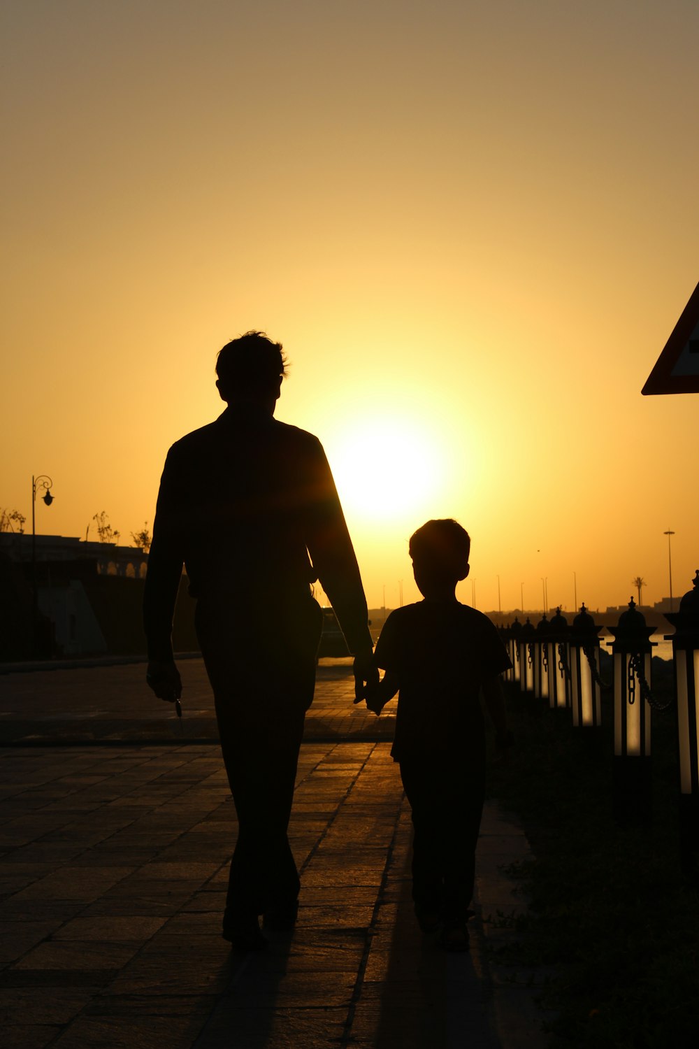 a man and a child walking down a sidewalk at sunset