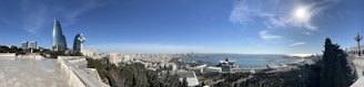 A panoramic view of a coastal city with green parks and modern buildings under a clear sky.