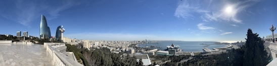 A panoramic view of a coastal city with green parks and modern buildings under a clear sky.