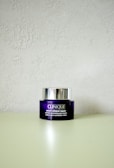 A Clinique smart clinical repair wrinkle correcting eye cream jar is placed on a light-colored surface. The jar is purple with a metallic silver lid, and the label text is in white.