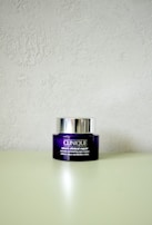 A Clinique smart clinical repair wrinkle correcting eye cream jar is placed on a light-colored surface. The jar is purple with a metallic silver lid, and the label text is in white.