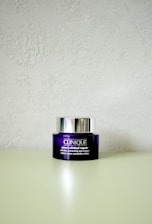 A Clinique smart clinical repair wrinkle correcting eye cream jar is placed on a light-colored surface. The jar is purple with a metallic silver lid, and the label text is in white.