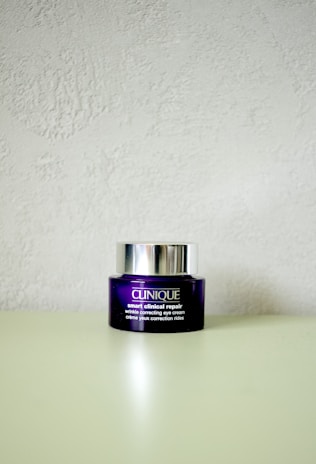 A Clinique smart clinical repair wrinkle correcting eye cream jar is placed on a light-colored surface. The jar is purple with a metallic silver lid, and the label text is in white.