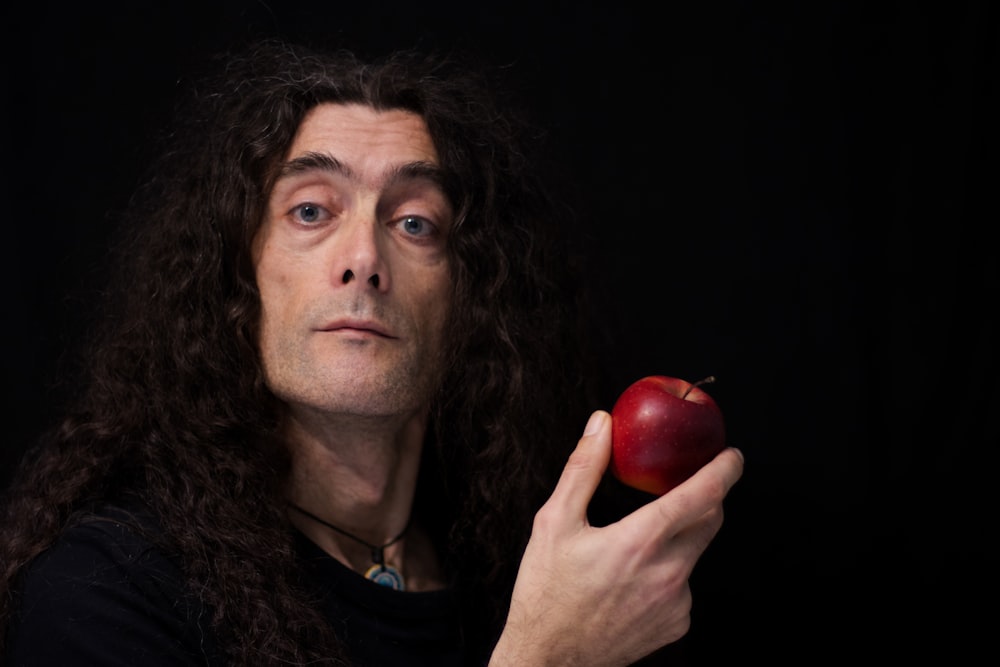 a man with long hair holding an apple