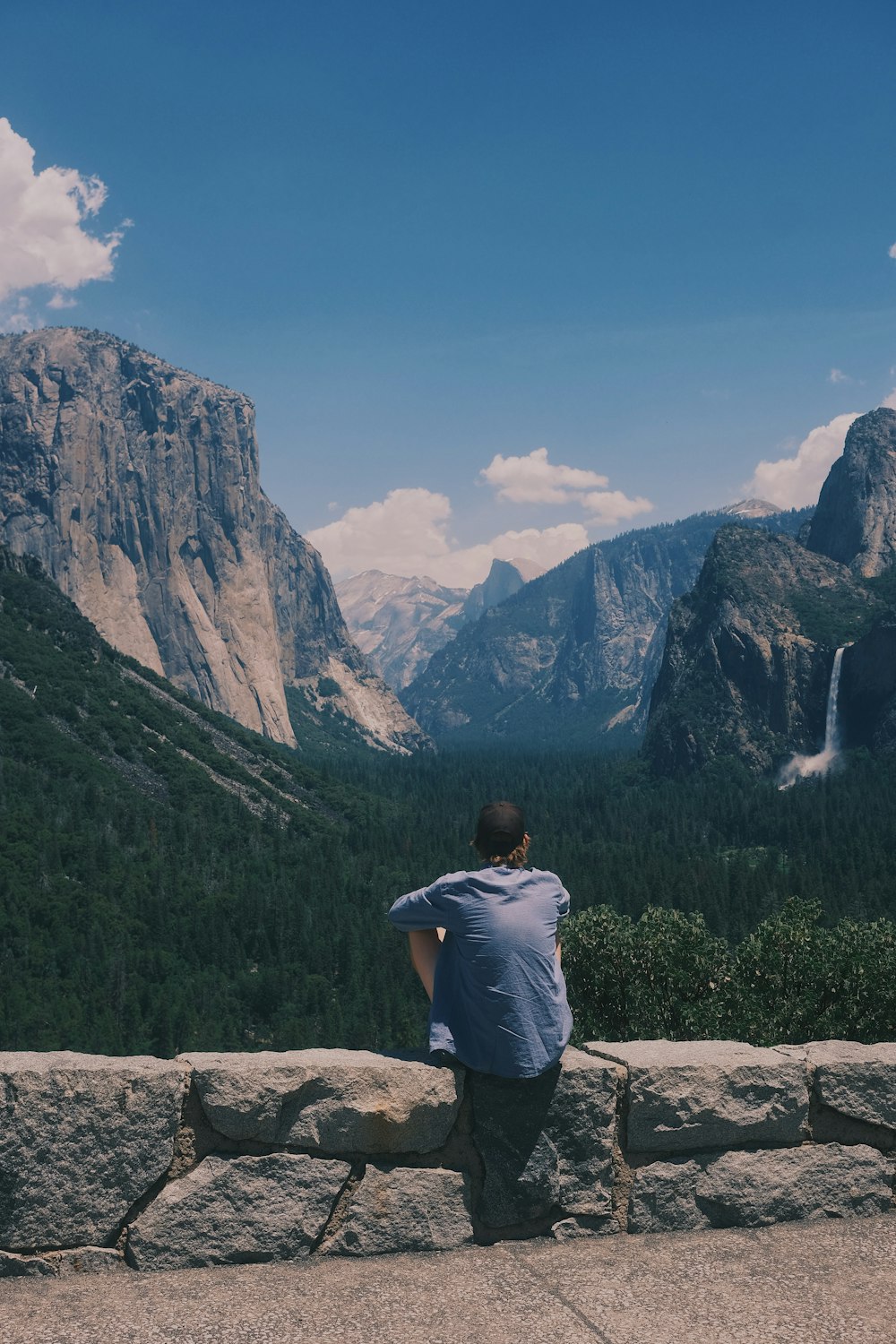 a man sitting on a stone wall looking at mountains