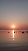A serene sunset view over calm waters with silhouettes of small boats.