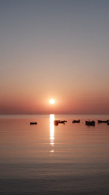 A serene sunset view over calm waters with silhouettes of small boats.