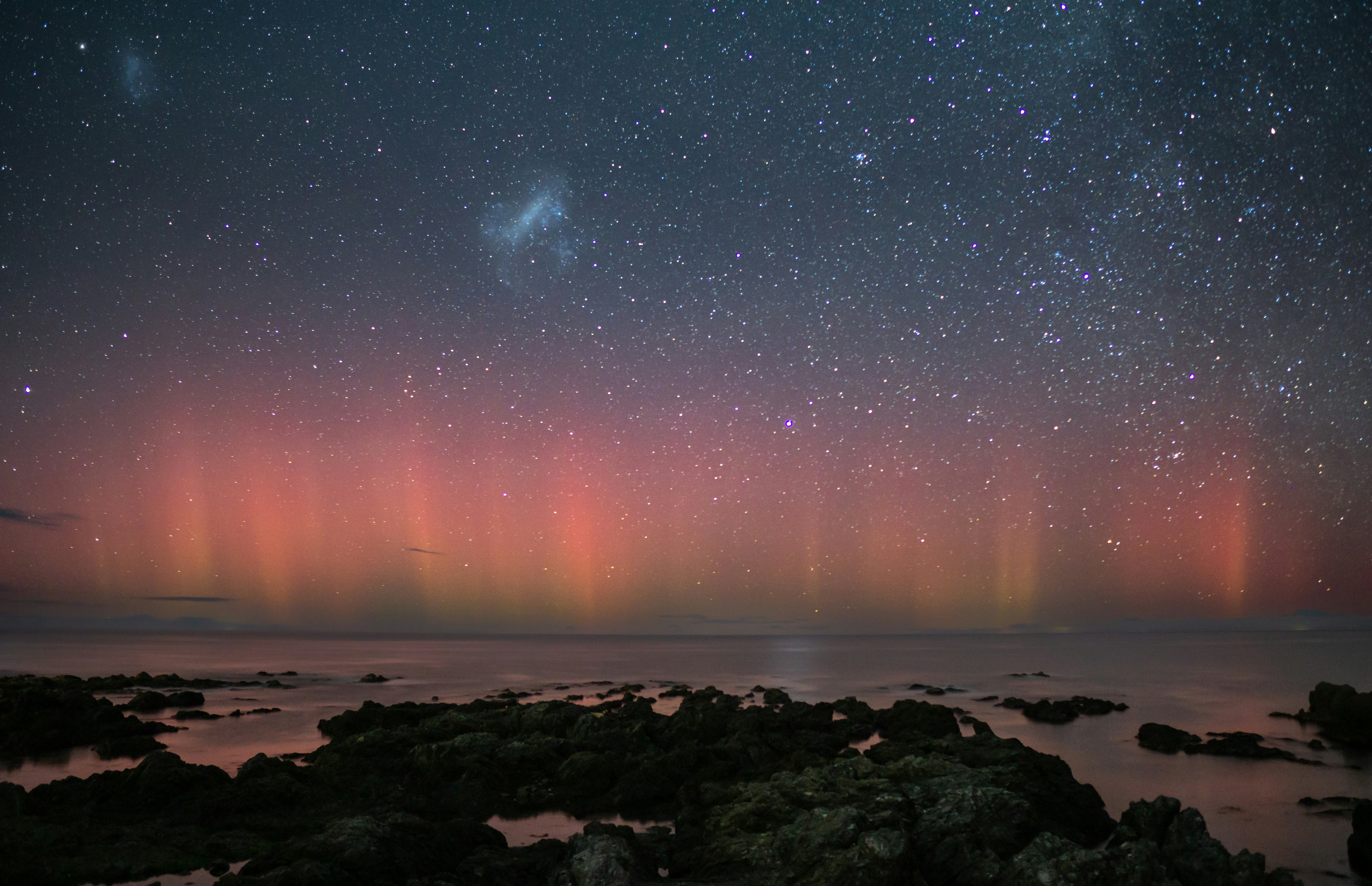 a view of the sky and the ocean from a rocky shore, It was winter, days before the new moon with a perfectly clear night sky, I had to go to the beach to take some pictures at the Milky Way. So I did, after a few minutes two friendly people in big 4x4 stopped by to ask me how clear my Sothern Lights shots were. My eyes glowed instantly, I took plenty of shots and this is the result.